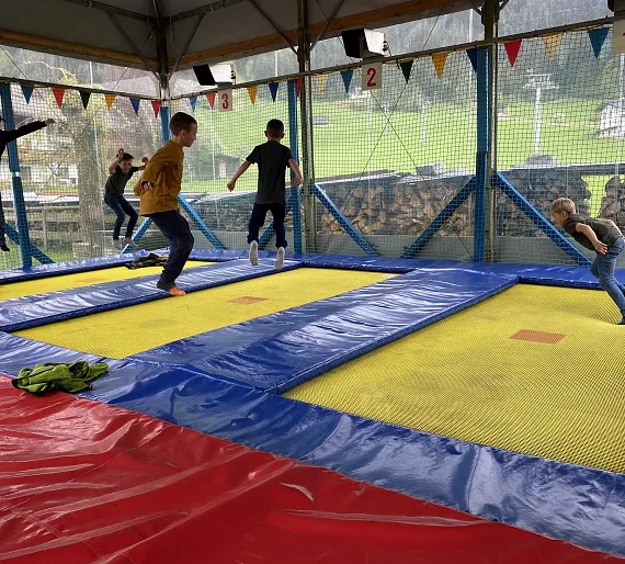 Kinder springen auf einem überdachten Trampolin in einer ländlichen Umgebung.