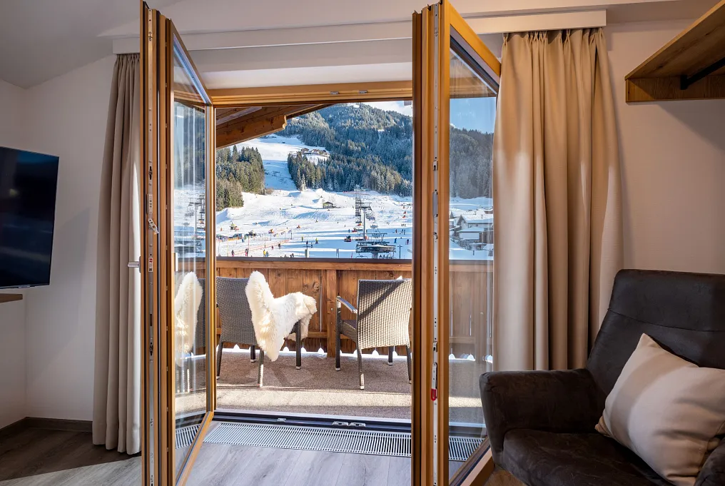 Blick von einer Hotelzimmerterrasse in Tirol auf schneebedeckte Berge und einen Skiort.