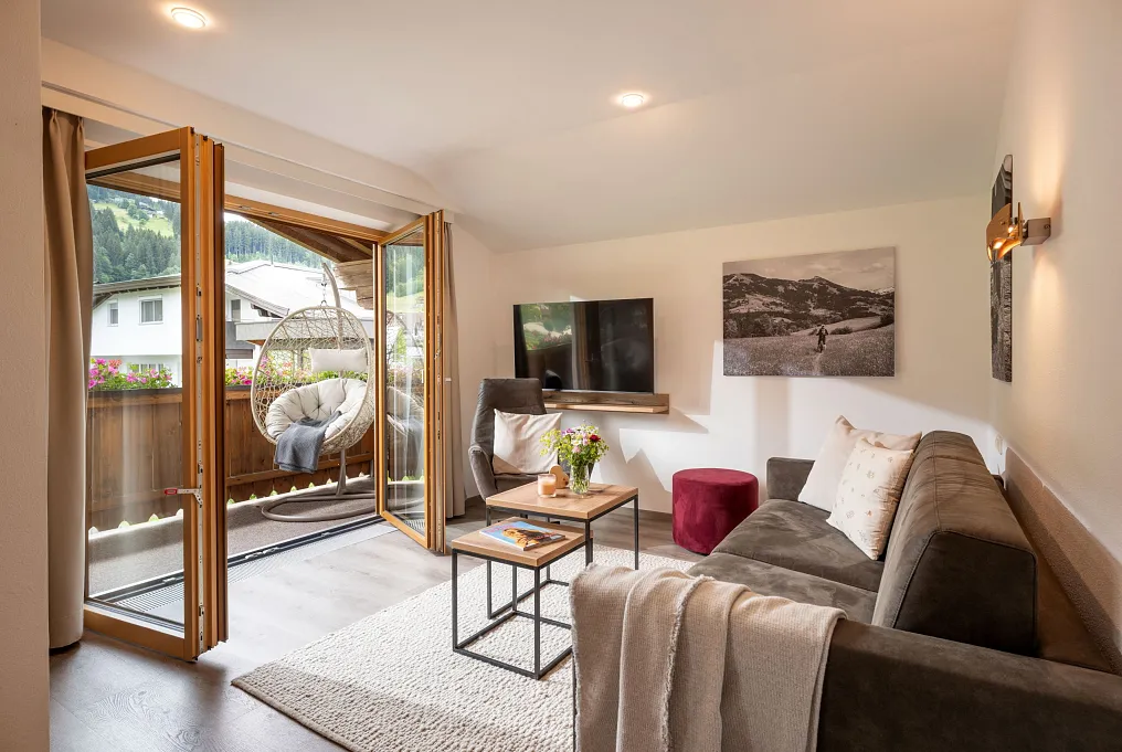 Modernes Wohnzimmer in Tirol mit Balkon, Couch, Hängesessel und Flachbildfernseher.