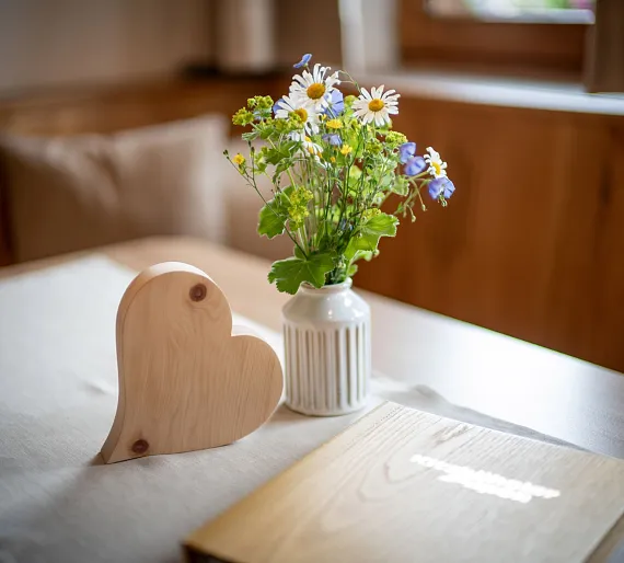 Vase mit Wildblumen und holzgeschnitztes Herz auf einem Tisch in einem gemütlichen Raum.
