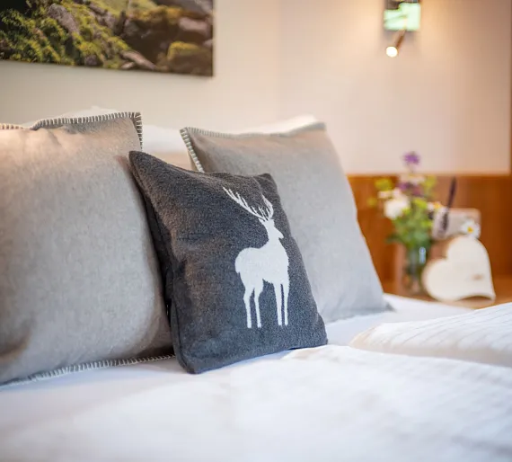 Modernes Schlafzimmer mit grauen Kissen und Hirschmotiv, im Hintergrund Blumen im Holzdekor.