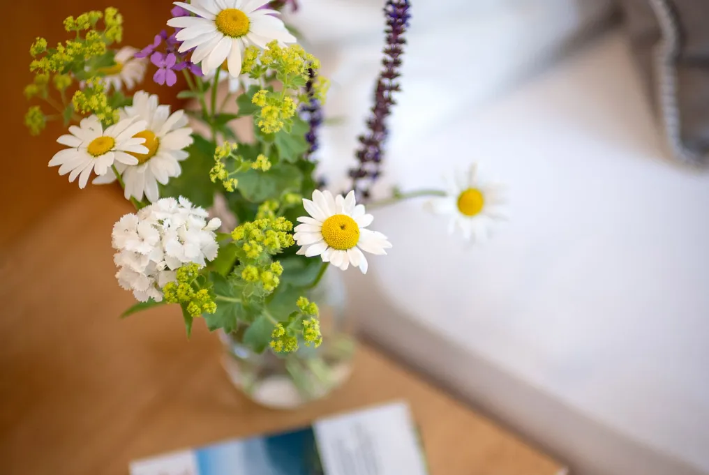 Blumenstrauß mit Margeriten und Wildblumen in einer Vase auf einem Holztisch.