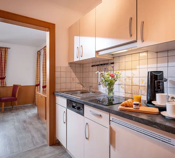 Moderne Küchenzeile in einer Ferienwohnung mit Kaffeemaschine, Saft und Croissants auf der Theke.