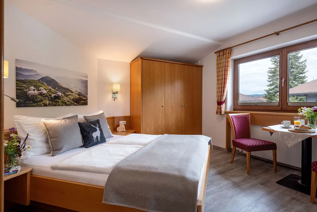 Gemütliches Hotelzimmer in Tirol mit Doppelbett, Holzmöbeln und Bergblick durch das Fenster.