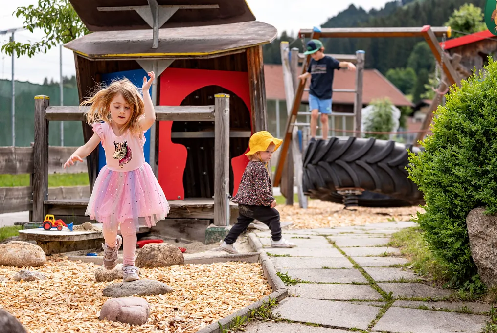 Kinder spielen auf einem Spielplatz mit Holzmulch und Spielgeräten im Freien.