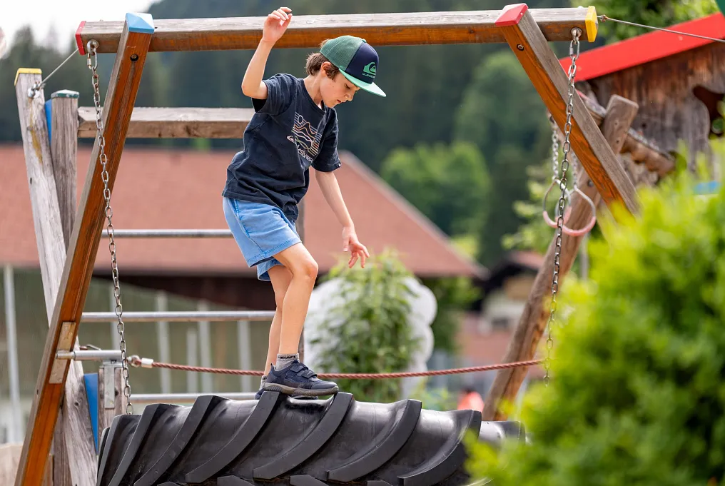 Kind balanciert auf Reifen in einem Spielplatz in ländlicher Umgebung.