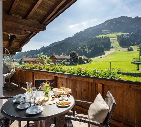 Frühstück auf einer sonnigen Terrasse mit Blick auf die Tiroler Berge und eine grüne Landschaft in Kitzbühel.