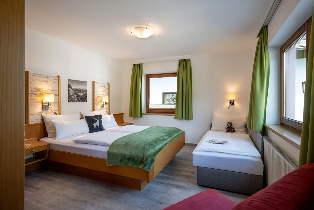 Helles Schlafzimmer mit einem Doppelbett und einem Einzelbett, dekoriert mit Naturmotiven an den Wänden.