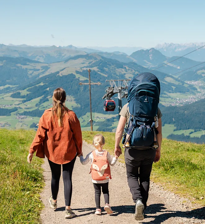 Familie wandert auf einem Bergpfad in Tirol mit Seilbahn im Hintergrund.