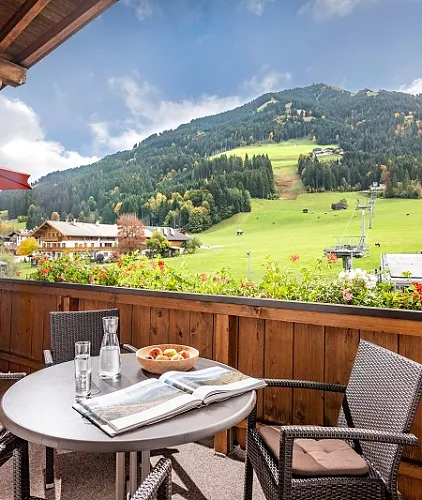 Blick von einer Terrasse auf grüne Hügel und Wälder in Kitzbühel, daneben ein Tisch mit Getränken und Obst.