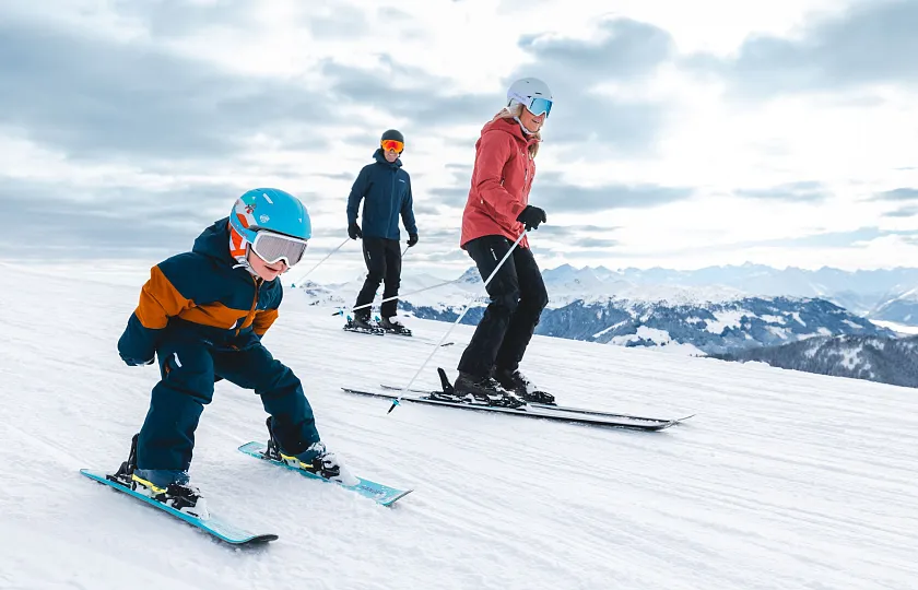 Drei Personen skifahren gemeinsam auf einer verschneiten Piste in einer Berglandschaft.