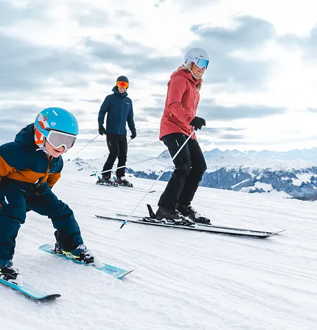 Drei Personen skifahren gemeinsam auf einer verschneiten Piste in einer Berglandschaft.