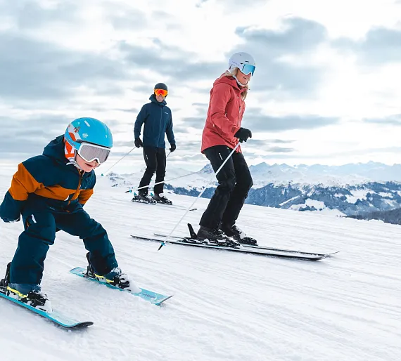 Drei Personen skifahren gemeinsam auf einer verschneiten Piste in einer Berglandschaft.
