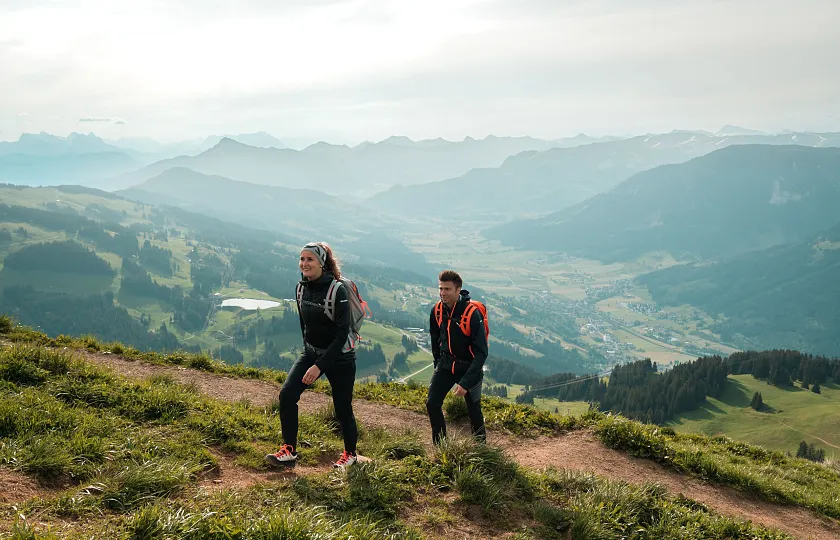 Zwei Menschen wandern auf einem Bergpfad mit Blick auf die Alpen in Kitzbühel.