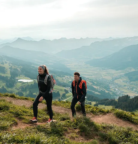 Zwei Menschen wandern auf einem Bergpfad mit Blick auf die Alpen in Kitzbühel.