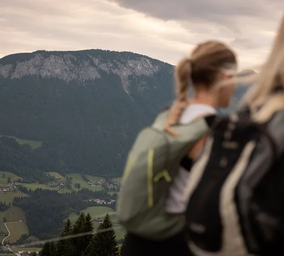 Zwei Personen mit Rucksäcken wandern in den Bergen von Tirol mit Bergpanorama im Hintergrund.